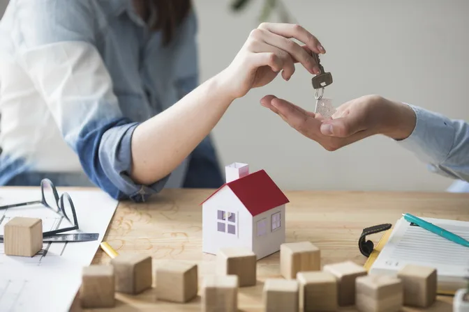Close Up Woman S Hand Giving House Key Man Wooden Table | SC REAL ESTATE ASSESSORS IMMOBILIARIS SL